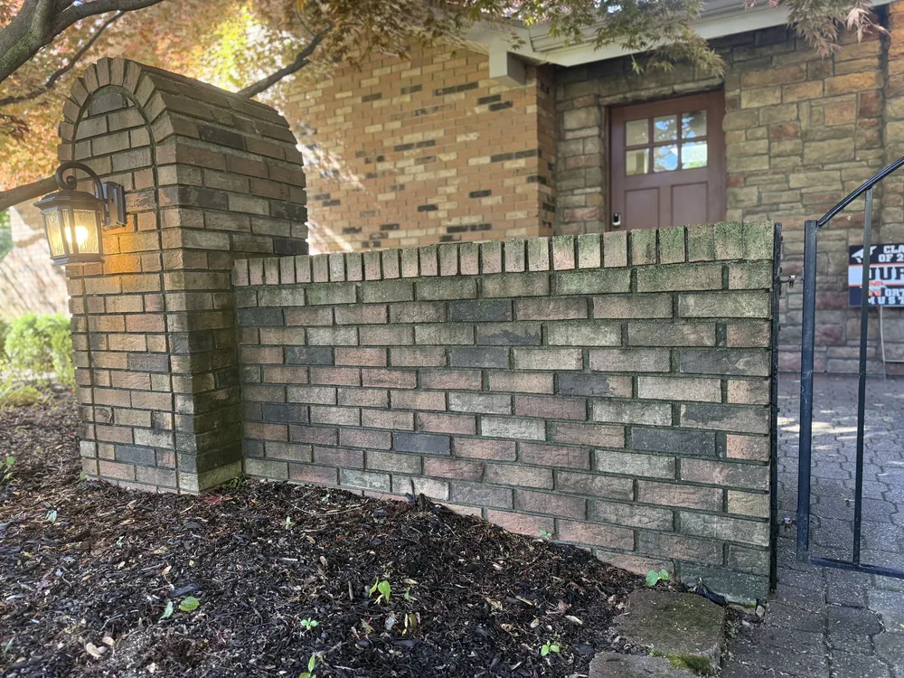 Brick wall and pillar in Northville covered in moss and algae before soft washing